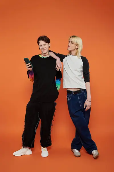 Two young friends, dressed in stylish vibrant attire, pose together against a bright orange background. — Stock Photo