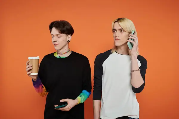 Two young queer friends pose in vibrant attire against an orange backdrop. — Stock Photo