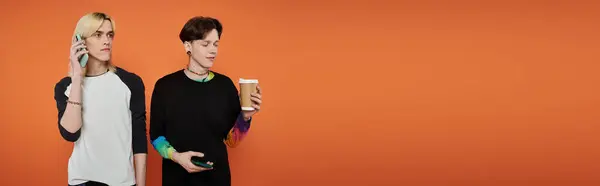 Dos jóvenes amigos con ropa elegante posan sobre un fondo naranja. - foto de stock