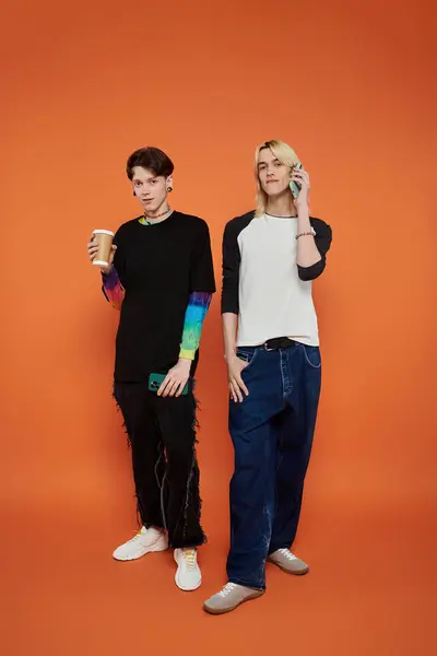 Two young friends wearing colorful outfits pose against an orange background. — Stock Photo