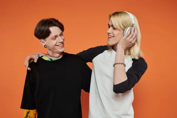 Two young queer friends, dressed in vibrant attire, pose together against a bright orange background. — Stock Photo