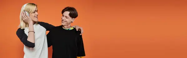 Two young queer people in vibrant attire pose against an orange background. — Stock Photo