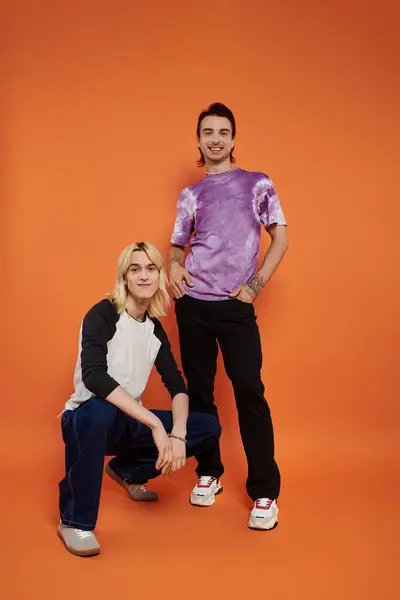 Two young queer friends strike a pose in colorful, stylish attire against an orange backdrop. — Stock Photo