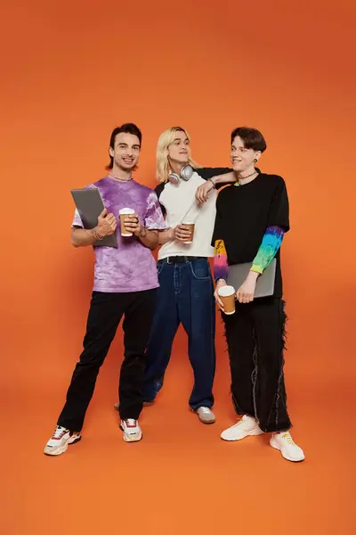 Three young queer friends pose together with coffee against a vibrant orange backdrop. — Stock Photo
