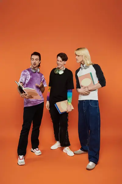 Three young friends, dressed in stylish, vibrant clothing, pose against an orange backdrop. — Stock Photo