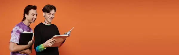 Два молодых странных друга в стильной улыбке во время чтения книг на оранжевом фоне. — стоковое фото