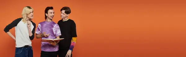 Three young friends in stylish attire stand against an orange background. They are engaged in a conversation. — Stock Photo