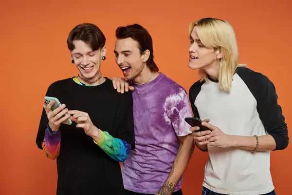 Three young friends in stylish, vibrant attire laugh together against an orange background. — Stock Photo