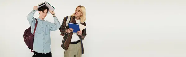 Двое молодых людей, одетых непринужденно, шутят с книгами на сером фоне. — стоковое фото