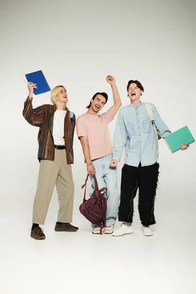 Three young, queer students celebrate their success in a casual setting, holding books and smiling. — Stock Photo