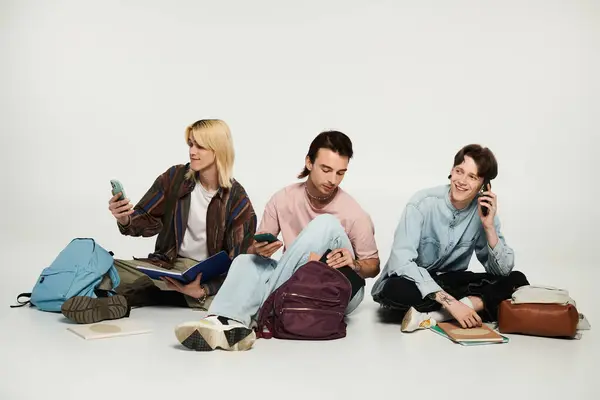 Three young students, part of the queer community, sit on a grey backdrop, using phones and enjoying each others company. — Stock Photo