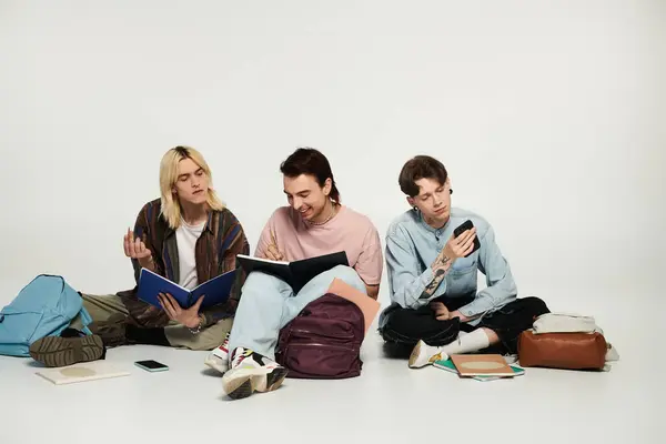 Tres jóvenes estudiantes queer se sientan en un fondo gris, estudiando y pasando el rato. — Stock Photo