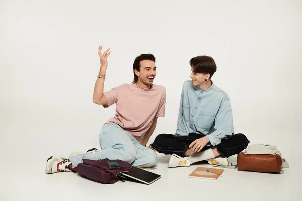 Two young queer students in casual attire laugh while sitting on the floor in a studio. — Stock Photo