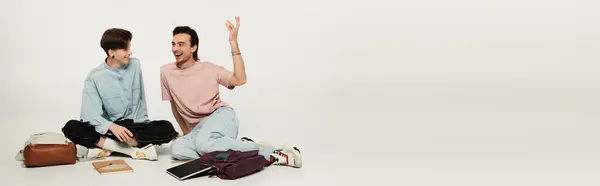 Two students in casual attire sit on the floor against a white backdrop, laughing and chatting, displaying their bond. — Stock Photo