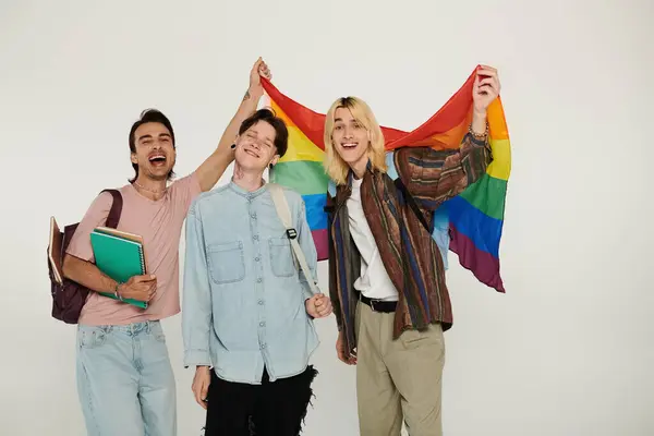 Three young students stand together, holding a rainbow flag, expressing their pride and unity as members of the LGBTQIA+ community. — Stock Photo