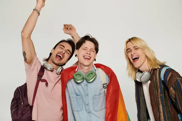 Tres jóvenes estudiantes, vestidos casualmente, posan con una bandera del arco iris y sonríen, celebrando su amistad e inclusión. — Stock Photo