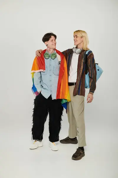 Dos jóvenes estudiantes se unen, una bandera arcoíris envuelta alrededor de ellos, en un gesto de amistad y apoyo a la comunidad LGBTQIA +. — Stock Photo