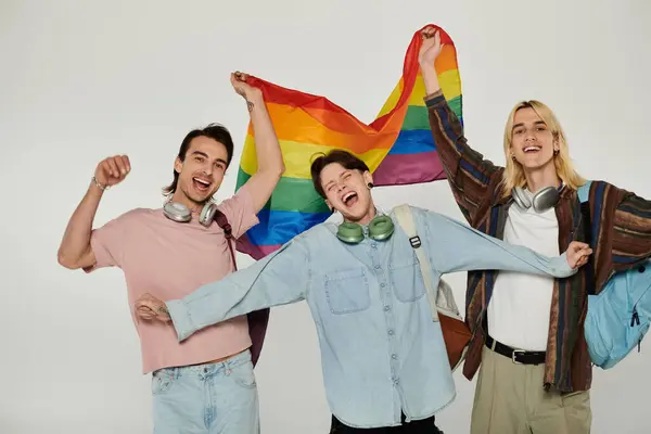 Three young students hold a rainbow flag and smile for the camera. — Stock Photo
