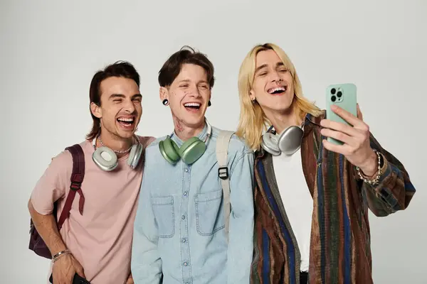 Three young, queer students laugh together while taking a selfie on a grey background. — Stock Photo