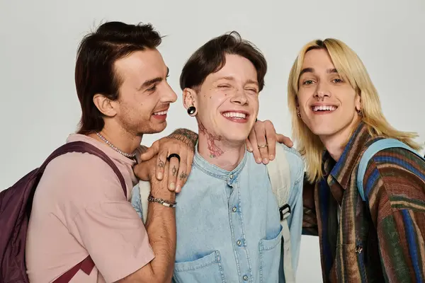 Three young queer students in casual attire stand together on a grey background, radiating joy and camaraderie. — Stock Photo