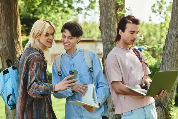 Drei junge Freunde stehen zusammen in einem Park, lächeln und schauen auf ein Telefon. — Stockfoto