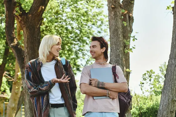 Two young friends, dressed casually, walk and talk in a park on a sunny day. — Stock Photo