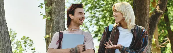 Two young friends, dressed casually, smile and talk to each other on a sunny day in the woods. — Stock Photo