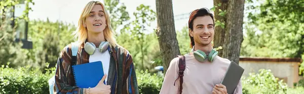 Dois jovens amigos vestindo trajes casuais caminham juntos através de um parque em um dia ensolarado. — Fotografia de Stock