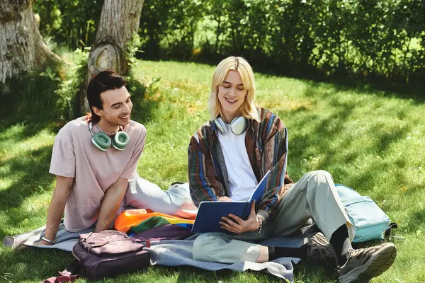 Two young friends, dressed in casual attire, sit on a blanket in a park, one reading a book while the other listens intently. — Stock Photo