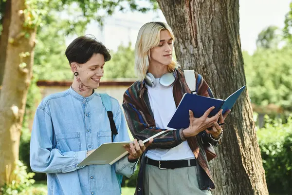 Two young friends, dressed casually, are studying together outdoors under a large tree. — Stock Photo