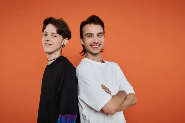 Dos amigos elegantes abrazan su individualidad contra un fondo naranja brillante, celebrando la comunidad LGBTQIA +. — Stock Photo