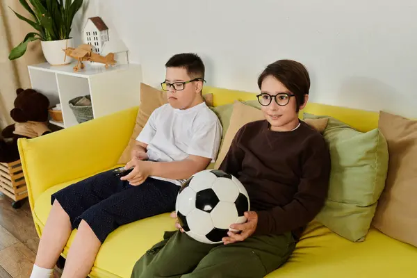 Dos niños pequeños, uno con síndrome de Down, están sentados en un sofá amarillo. — Stock Photo