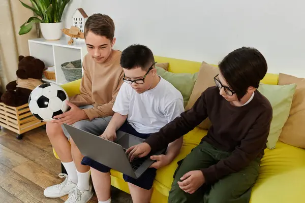 Três meninos, um com síndrome de Down, se divertir com um laptop e bola de futebol. — Stock Photo