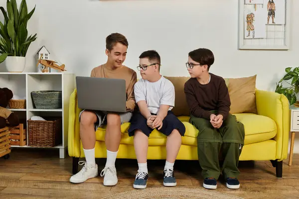 Three boys, including one with Down syndrome, share a laptop on a yellow couch in a home setting. — Stock Photo