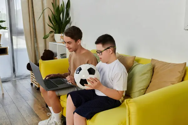 Two boys, one with Down syndrome, relax at home with a laptop and a soccer ball. — Stock Photo