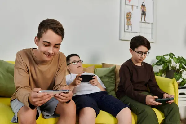 Three boys, including one with Down syndrome, sit on a yellow couch playing mobile games. — Stock Photo