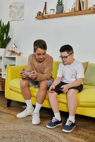 Two boys, one with Down syndrome, are playing video games on a yellow couch at home. — Stock Photo