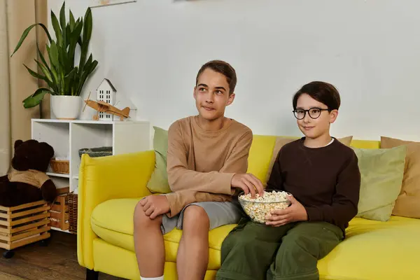 Два мальчика сидят на жёлтом диване, наслаждаясь попкорном вместе. — стоковое фото