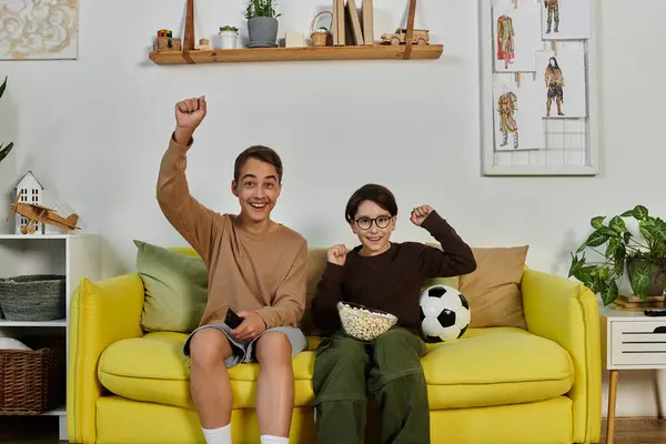 Dos chicos celebran en un sofá amarillo. - foto de stock