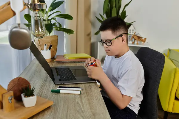A young boy with Down syndrome sits at his desk at home, concentrating on a Rubiks cube. — Stock Photo