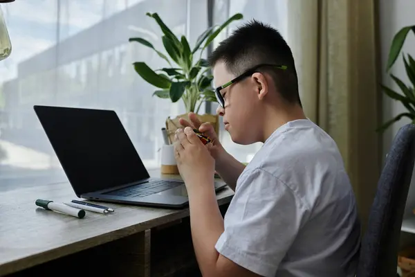 A young boy with Down syndrome sits at a desk in his home, focused on a task. — Stock Photo