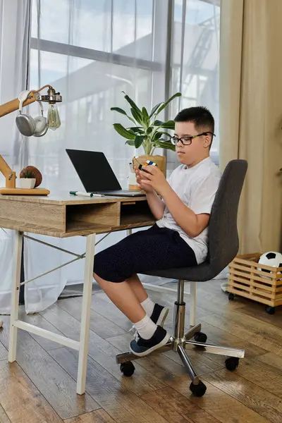 A young boy with Down syndrome sits at a desk, playing at home. — Stock Photo