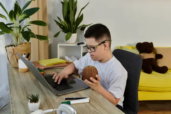 A young boy with Down syndrome sits at a desk at home using a laptop. — Stock Photo