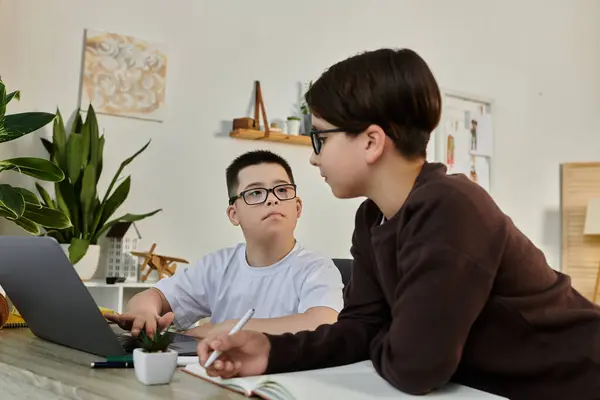 Two young boys work together at home, one using a laptop and the other writing in a notebook. — Stock Photo