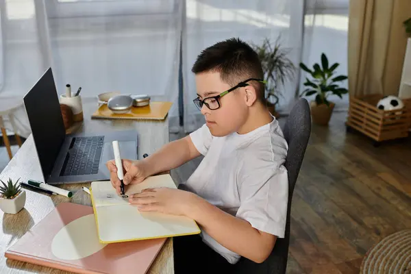 A young boy with Down syndrome sits at his desk, concentrating on drawing. — Stock Photo