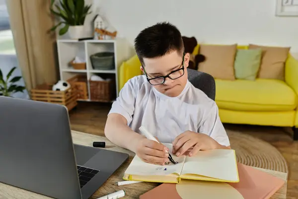Ein kleiner Junge mit Down-Syndrom sitzt an einem Tisch in seinem Haus und konzentriert sich auf seine Arbeit. — Stockfoto