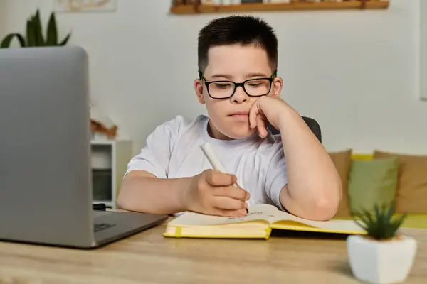 A young boy with Down syndrome concentrates on his schoolwork at home. — Stock Photo