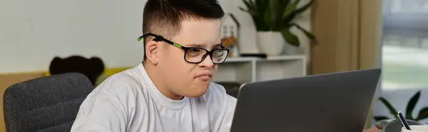 A young boy with Down syndrome sits at a desk, intently looking at his laptop. — Stock Photo