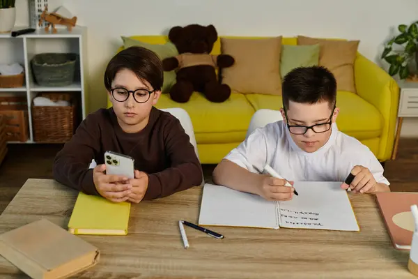 Zwei Jungen, einer mit Down-Syndrom, zu Hause, einer telefoniert, einer schreibt in Notizbuch. — Stockfoto