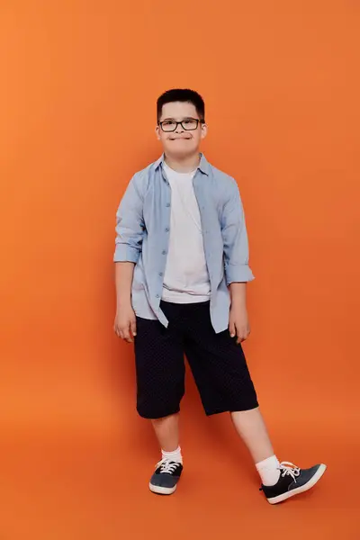 A young boy with Down syndrome poses confidently against a vibrant orange background. — Stock Photo